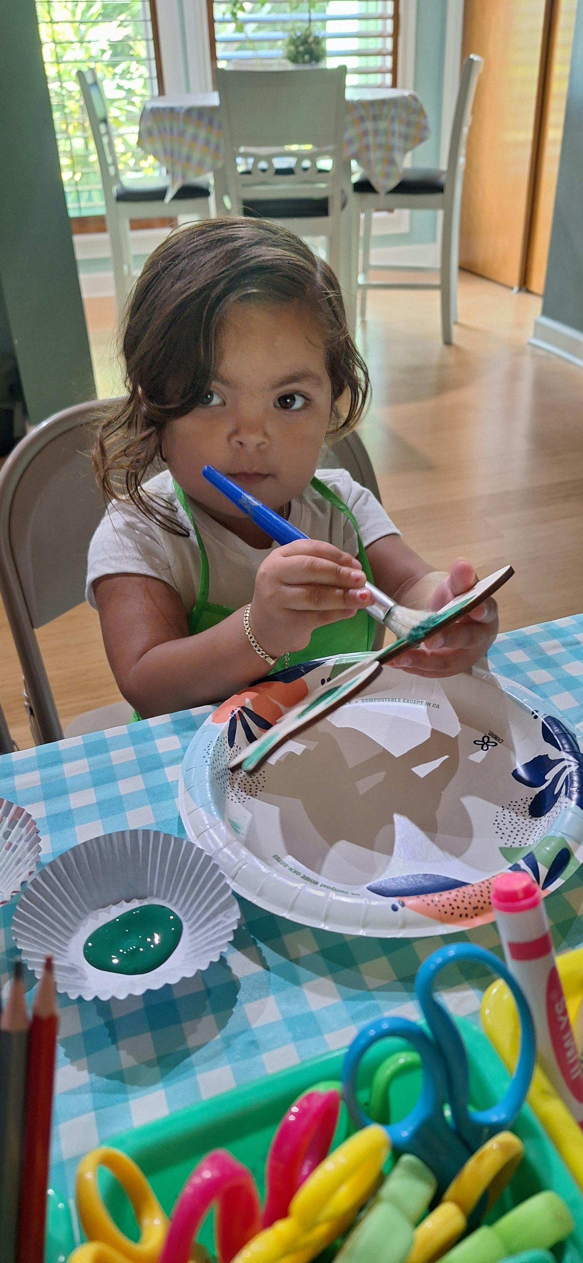 Child painting a wooden shape at a table
