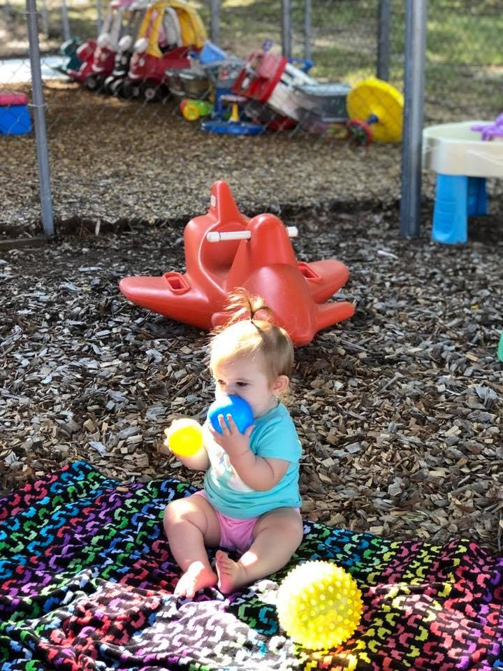 Child sitting on a colorful blanket, holding a blue ball to their mouth