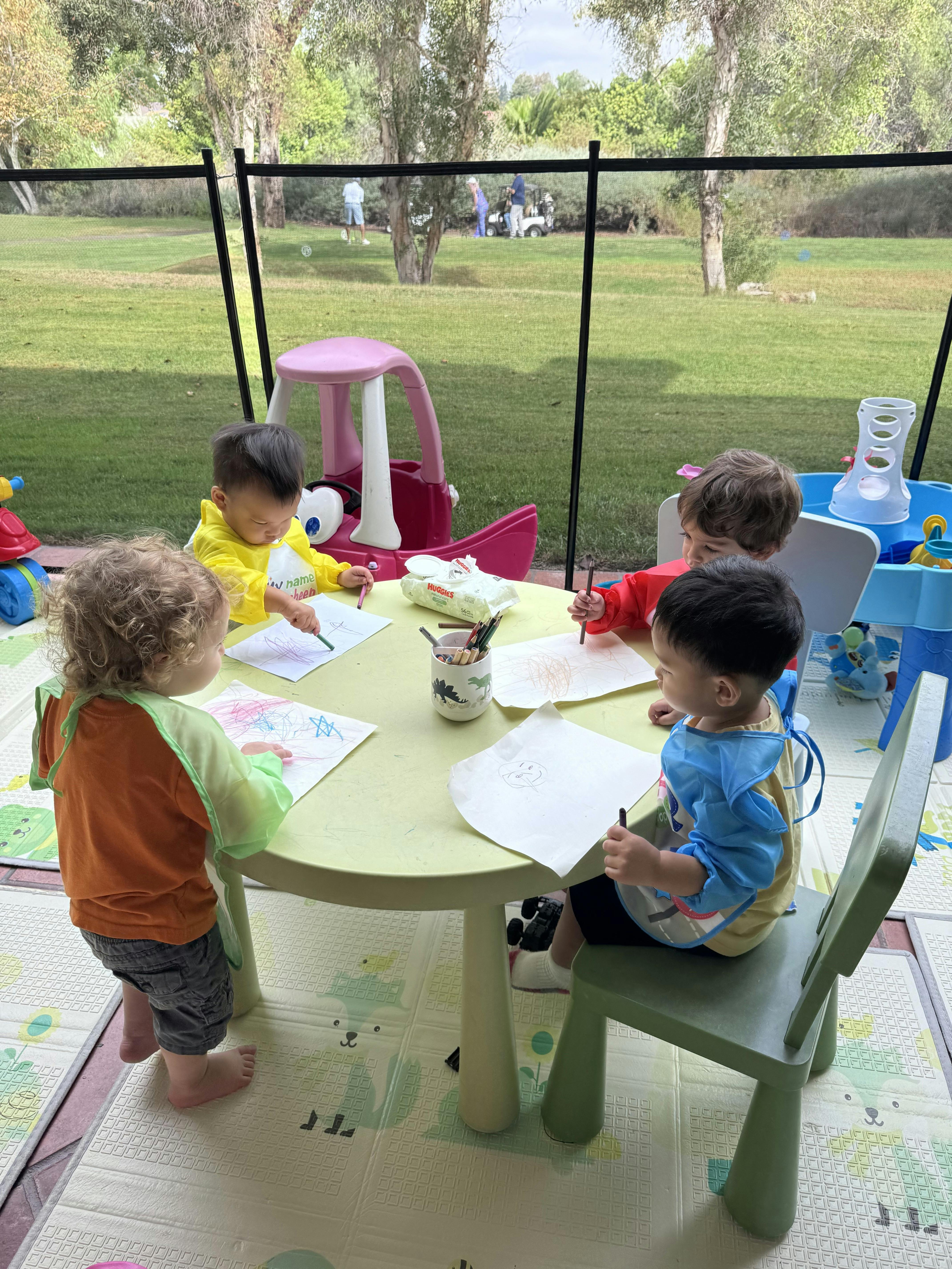 Four children sitting and standing around a table drawing with markers