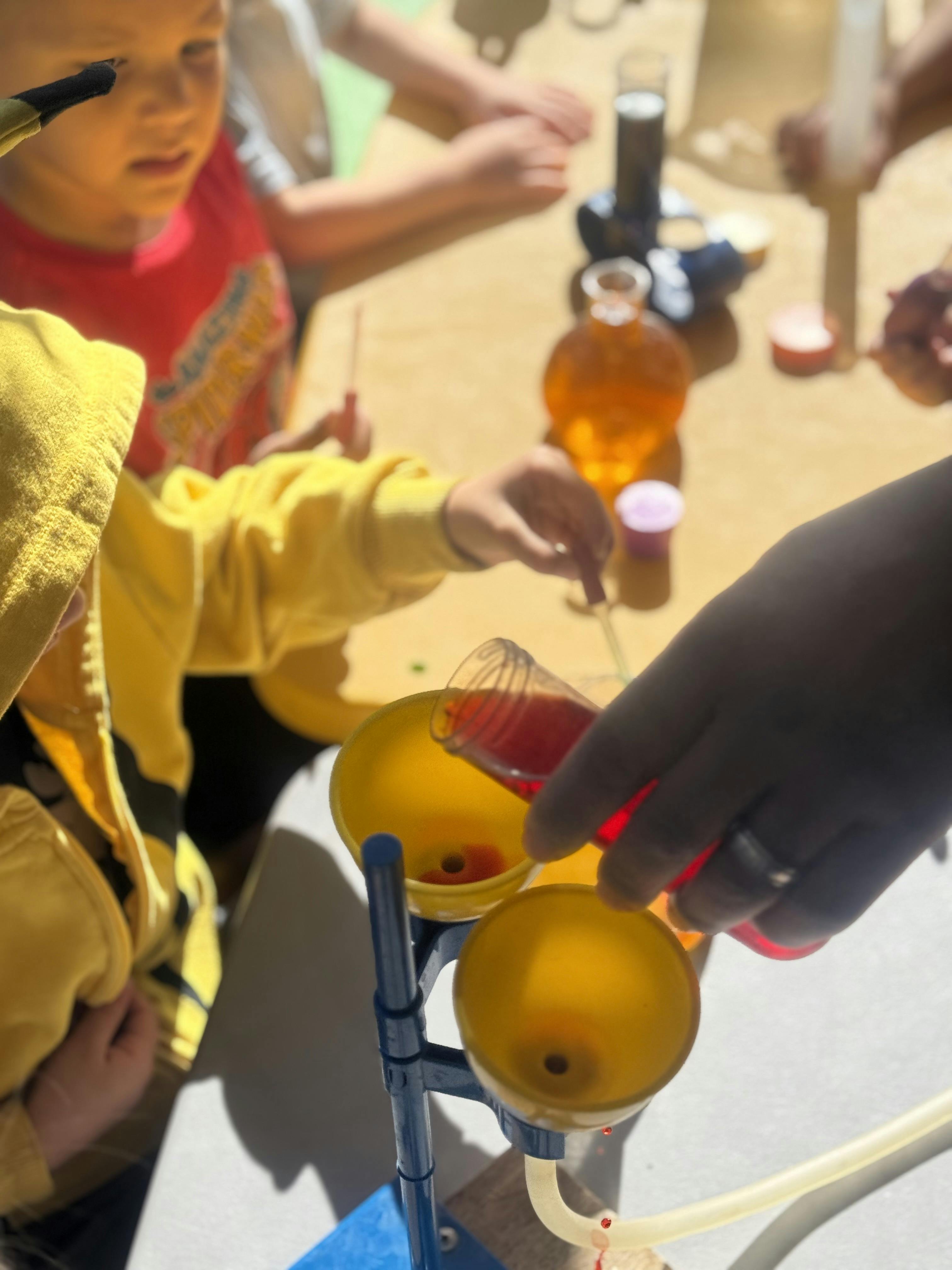 Person pouring red liquid from a beaker into a yellow funnel