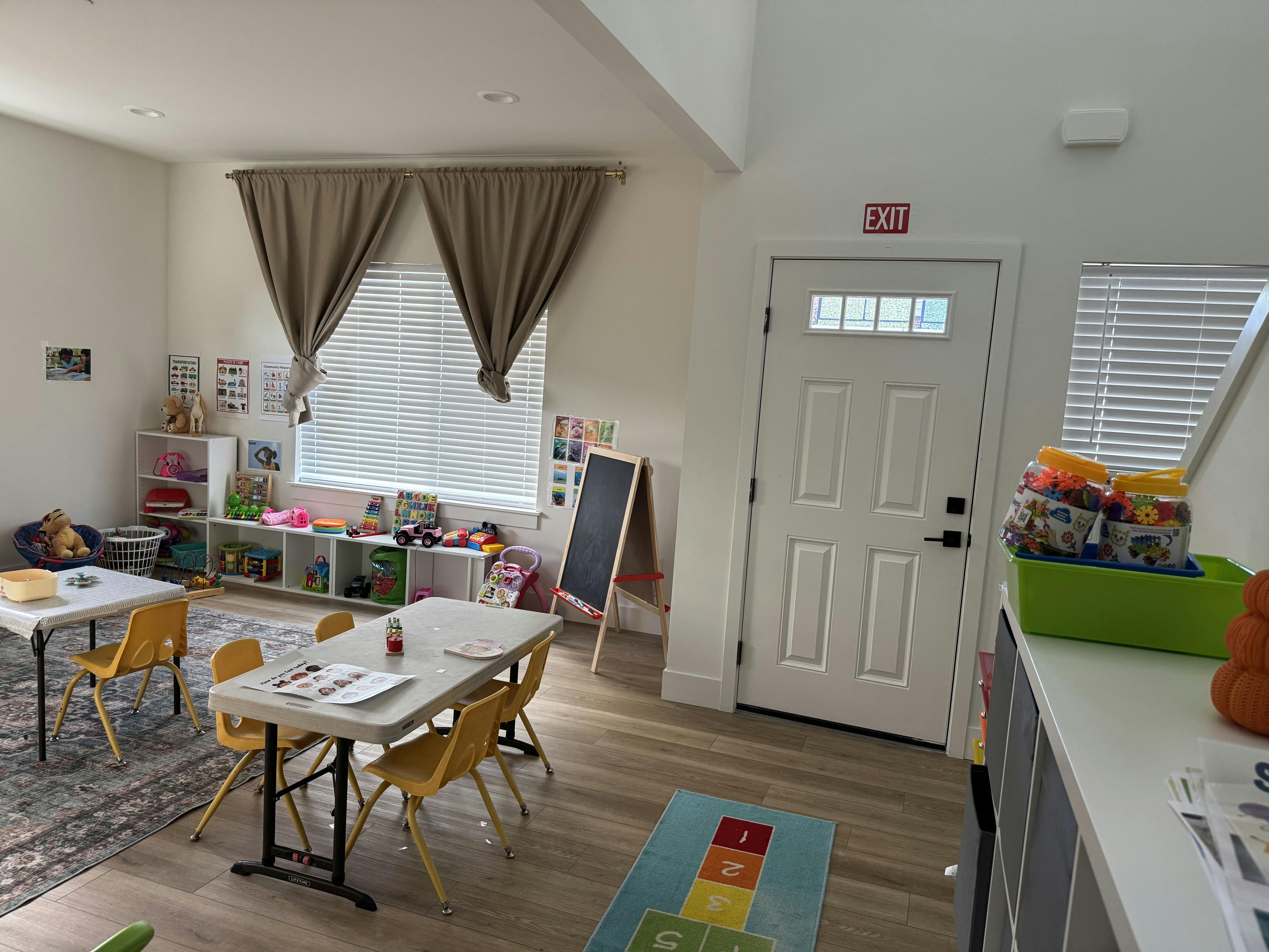 Classroom with child-sized tables and chairs, shelves of toys, and a chalkboard