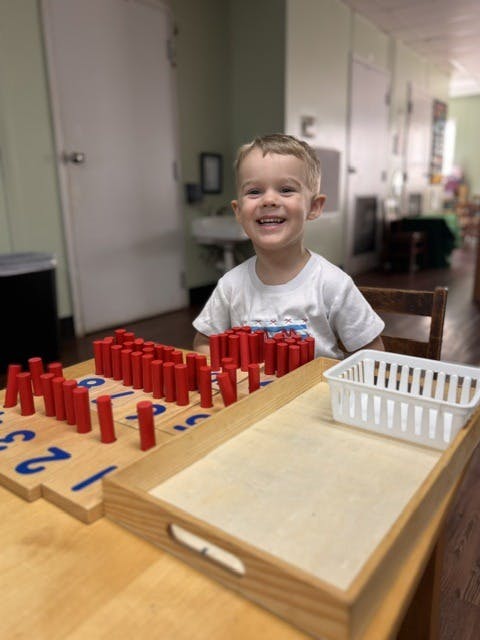 Child playing with wooden counting rods and a numbered board