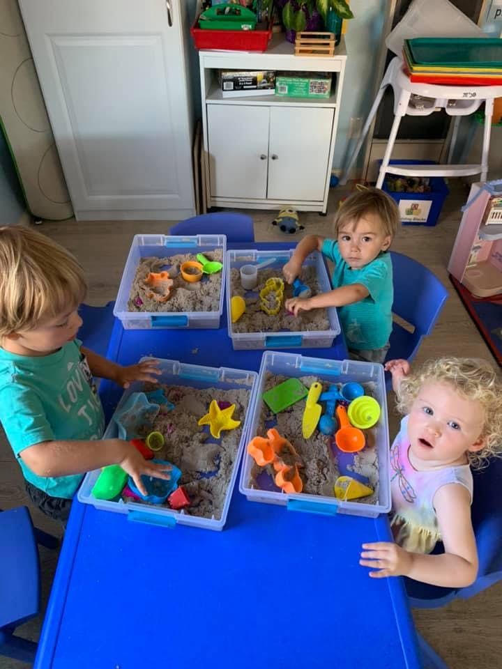 Three children playing with kinetic sand at a blue table