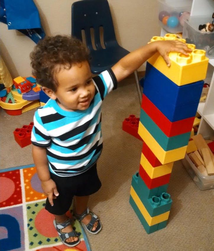 Child standing next to a tall stack of colorful building blocks