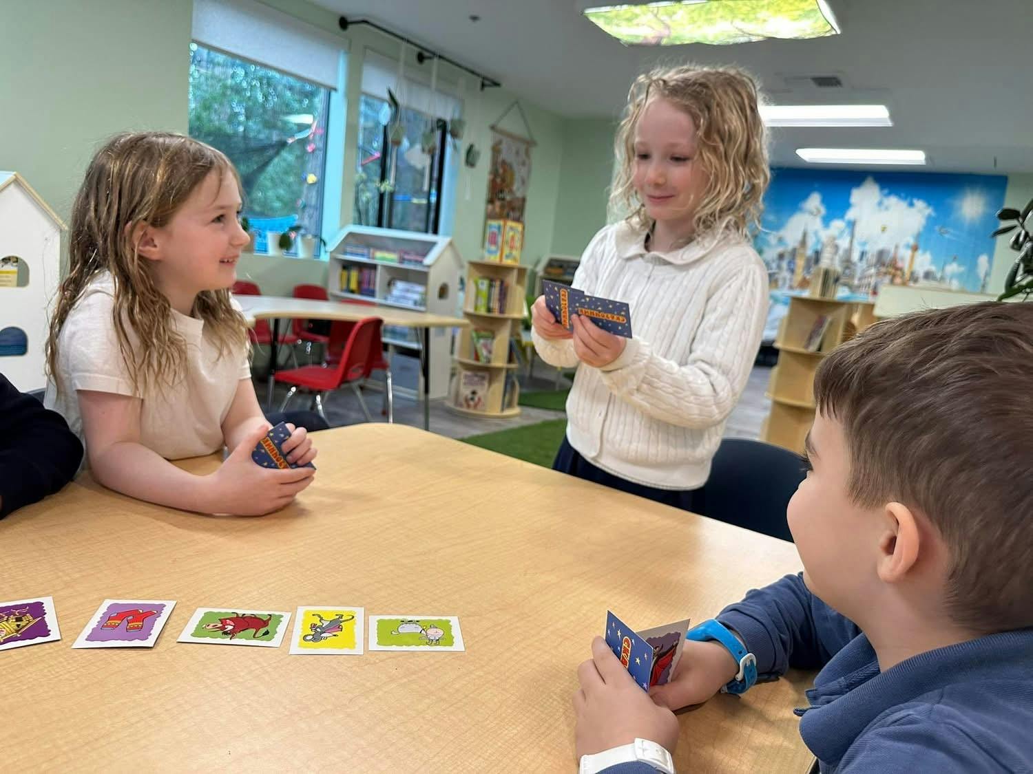 Three children playing a card game at a table in a classroom
