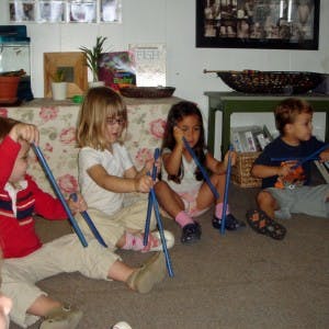Four children sitting on the floor playing with blue sticks