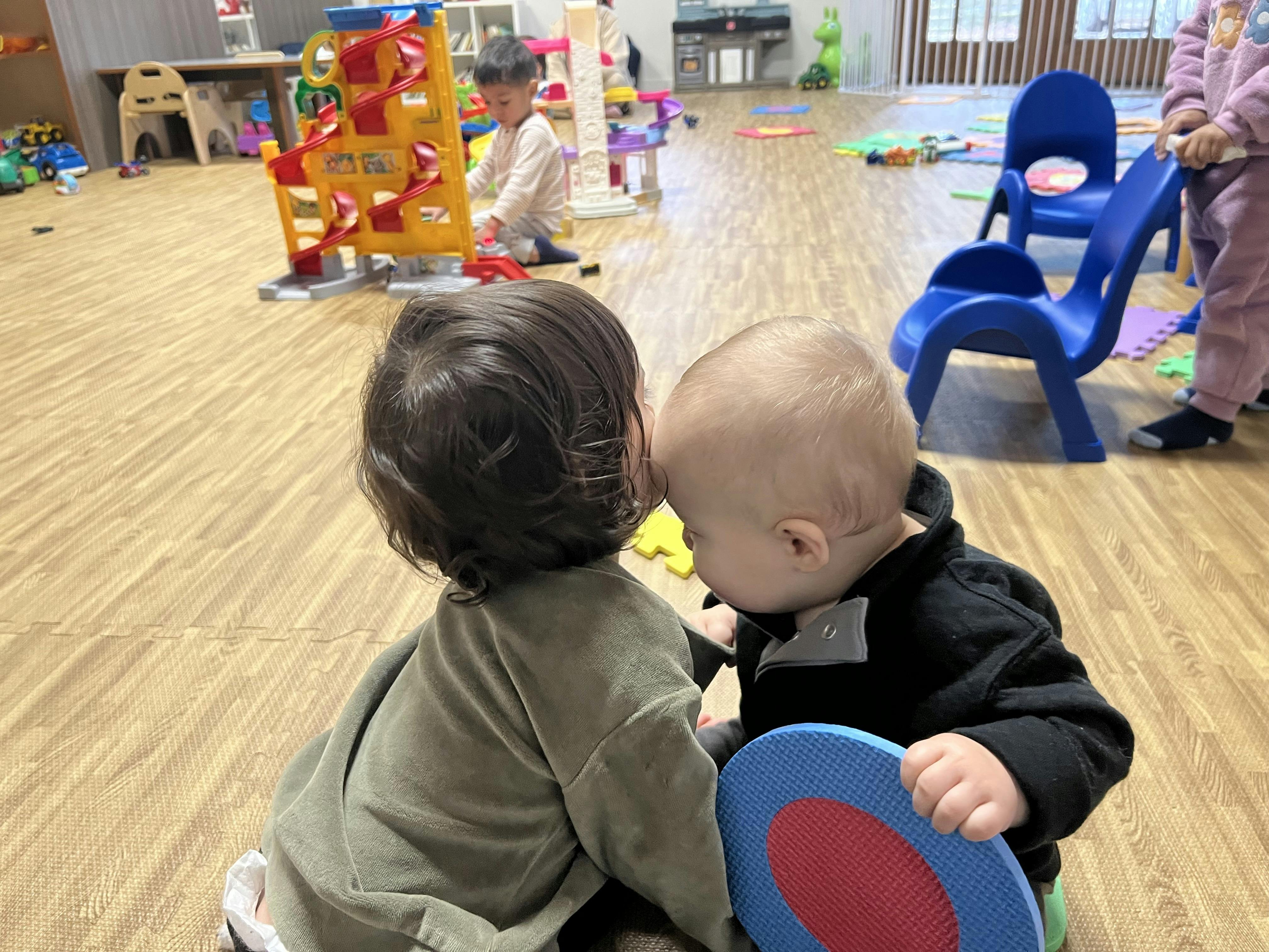 Two children playing together on a wooden floor in a classroom