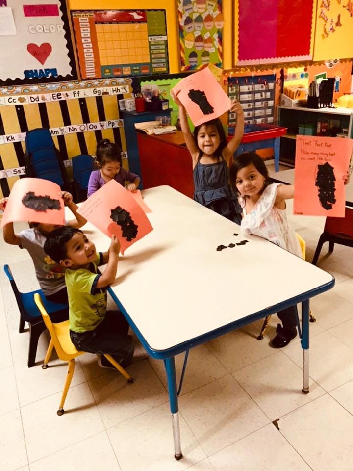 Children holding up artwork with black footprints in a classroom