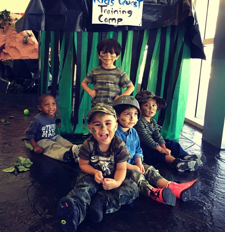 Five children in camouflage clothing and face paint sitting in front of a tent