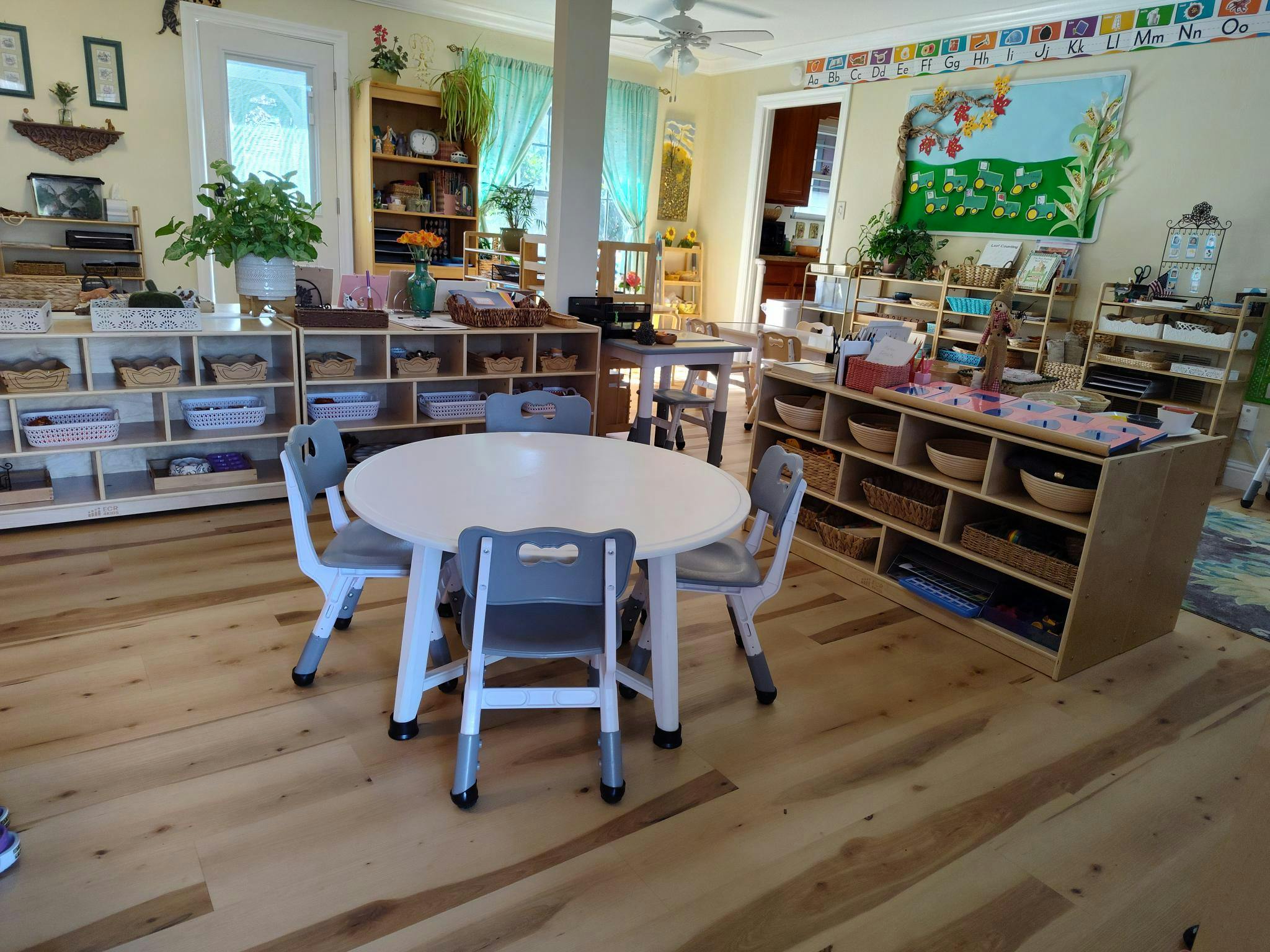 Classroom with small tables and chairs, shelves with baskets, and educational decorations
