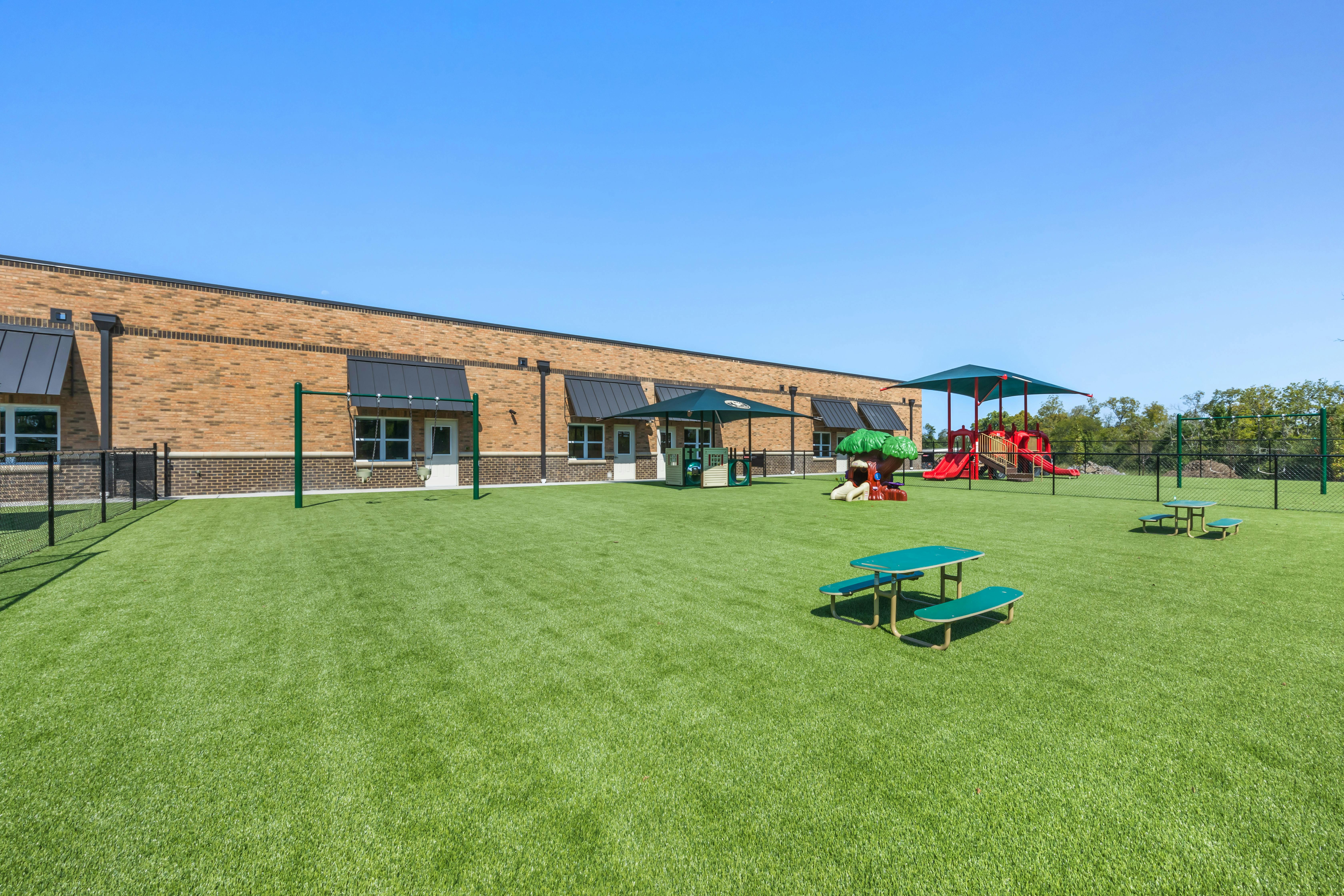 An outdoor playground with artificial turf, play structures, and small picnic tables