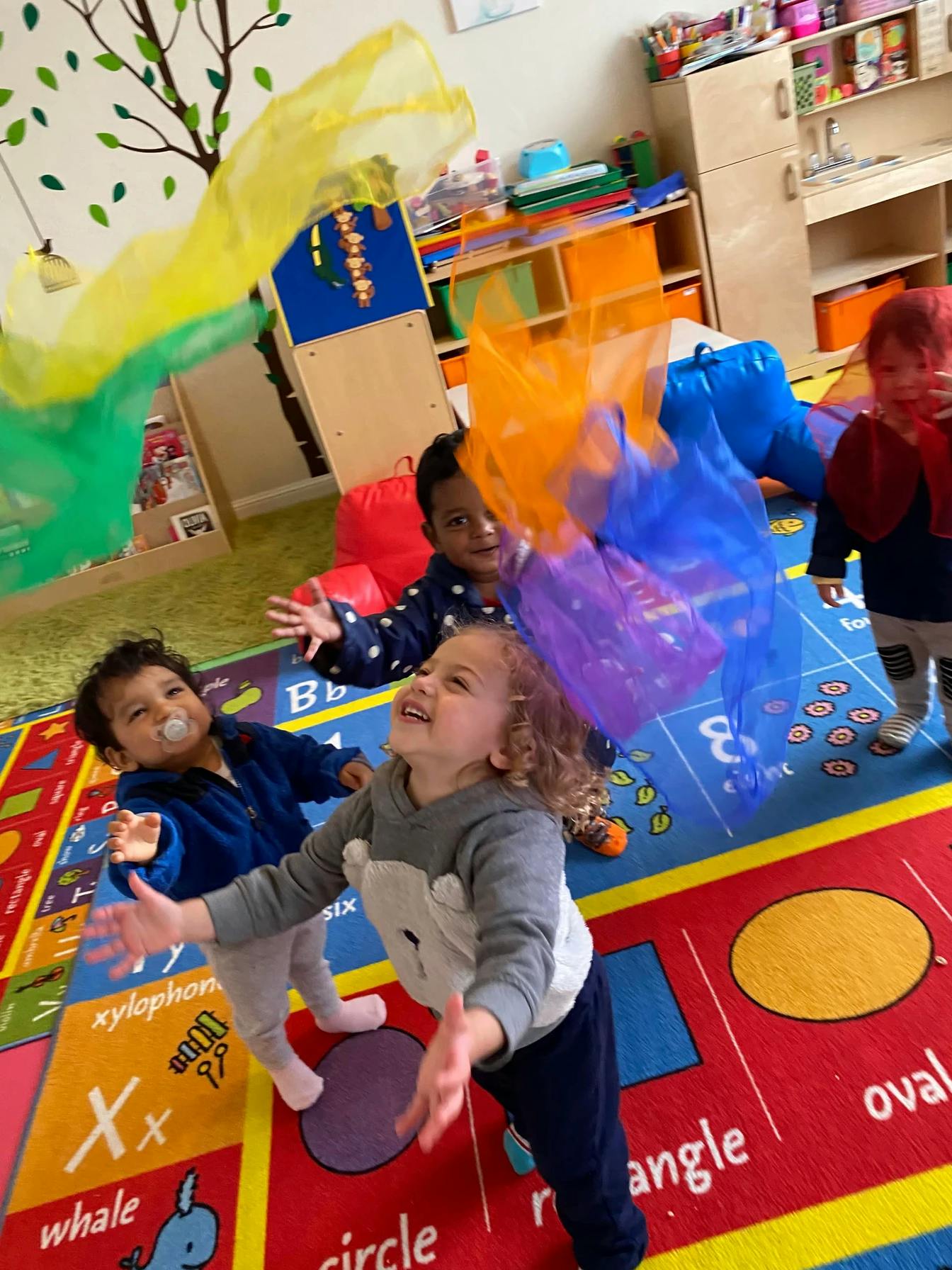 Children playing with colorful sheer fabrics in a classroom