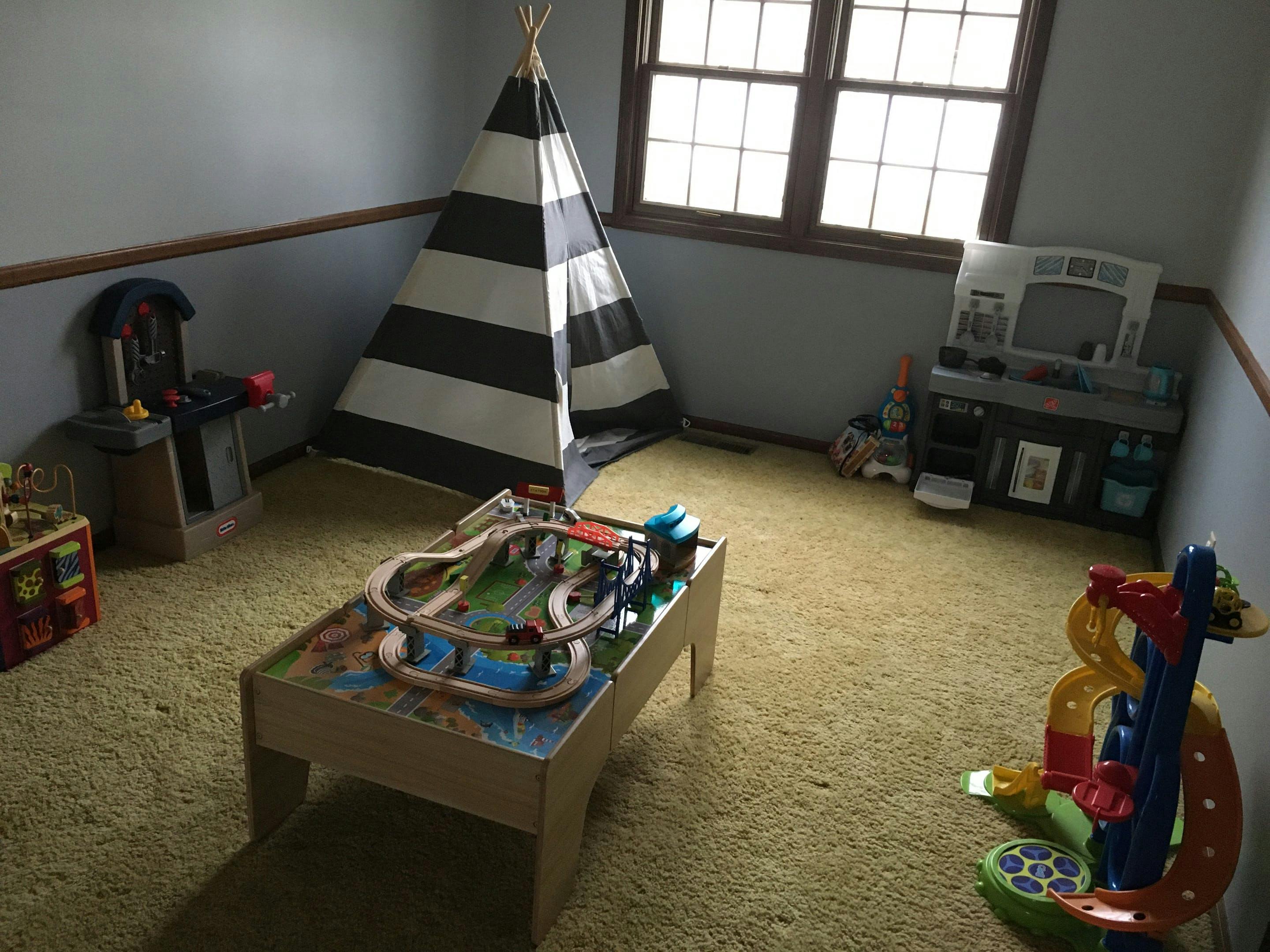 Playroom with a striped teepee, toy kitchen, and train table