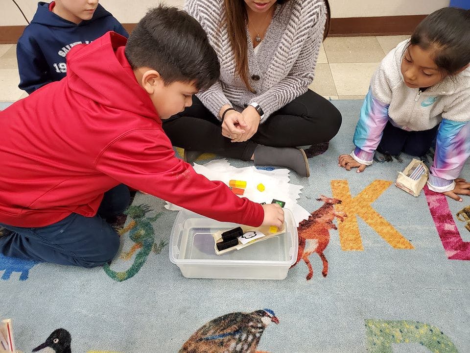 Child in red shirt playing with items in a clear bin with other people