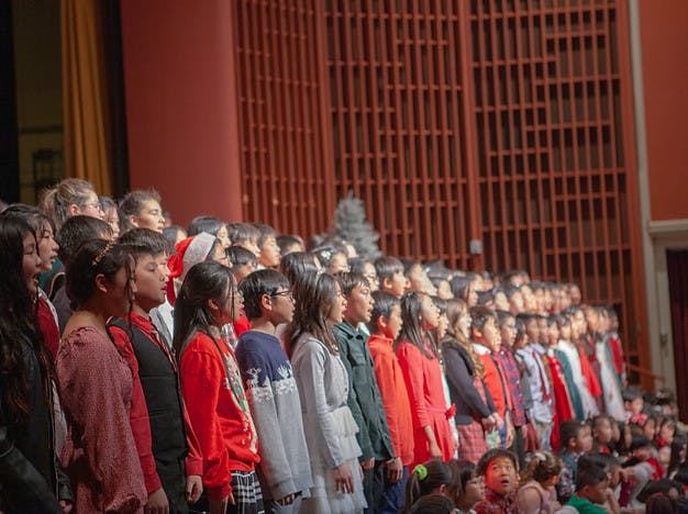 Group of children and teens standing on stage, singing in a choir