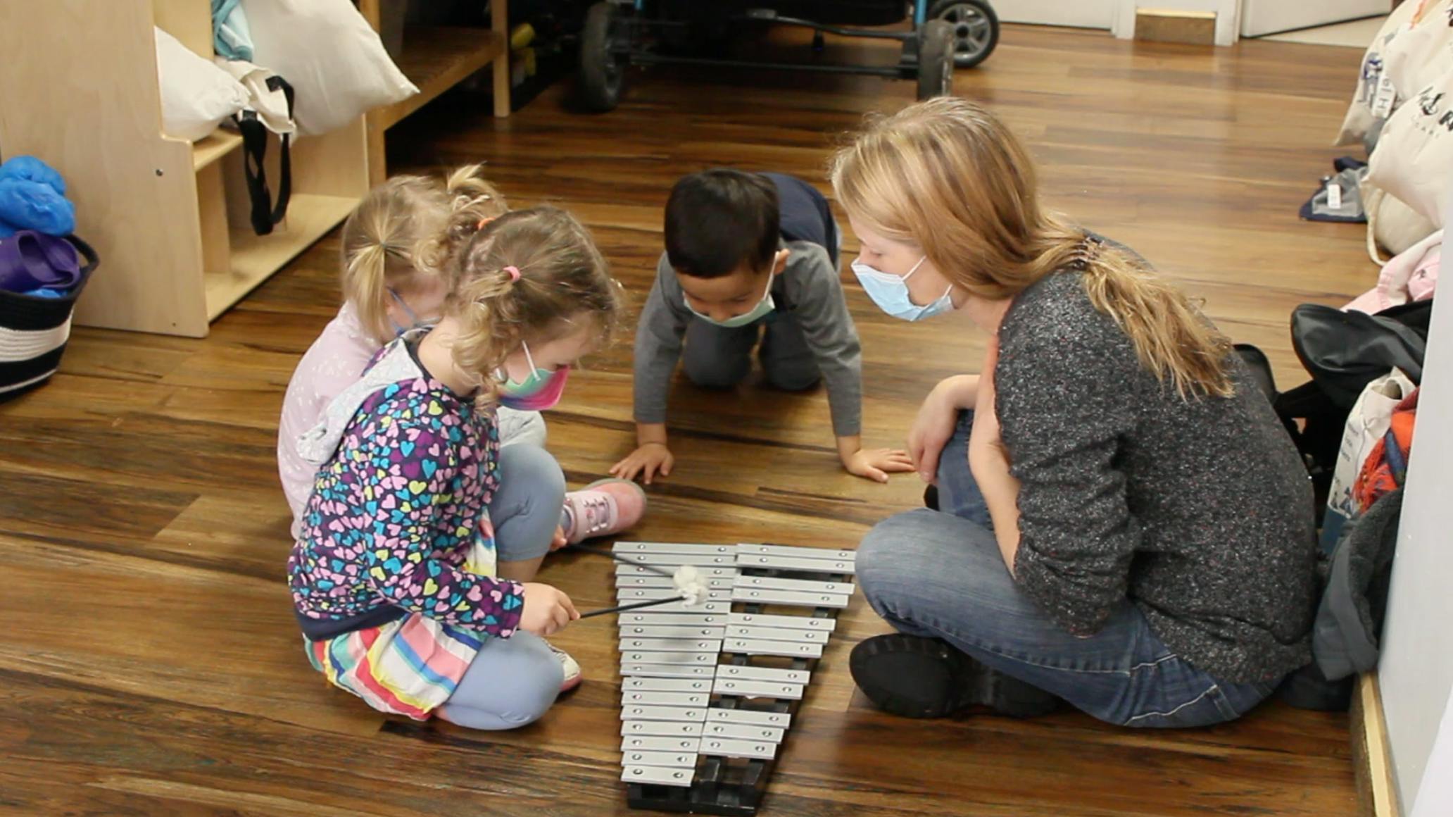 Adult and three children on floor playing with a xylophone