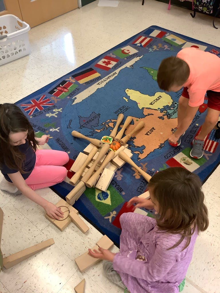 Three children playing with wooden blocks and mallets on a world map rug