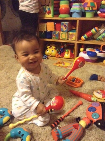 Child sitting on a rug holding a red toy maraca