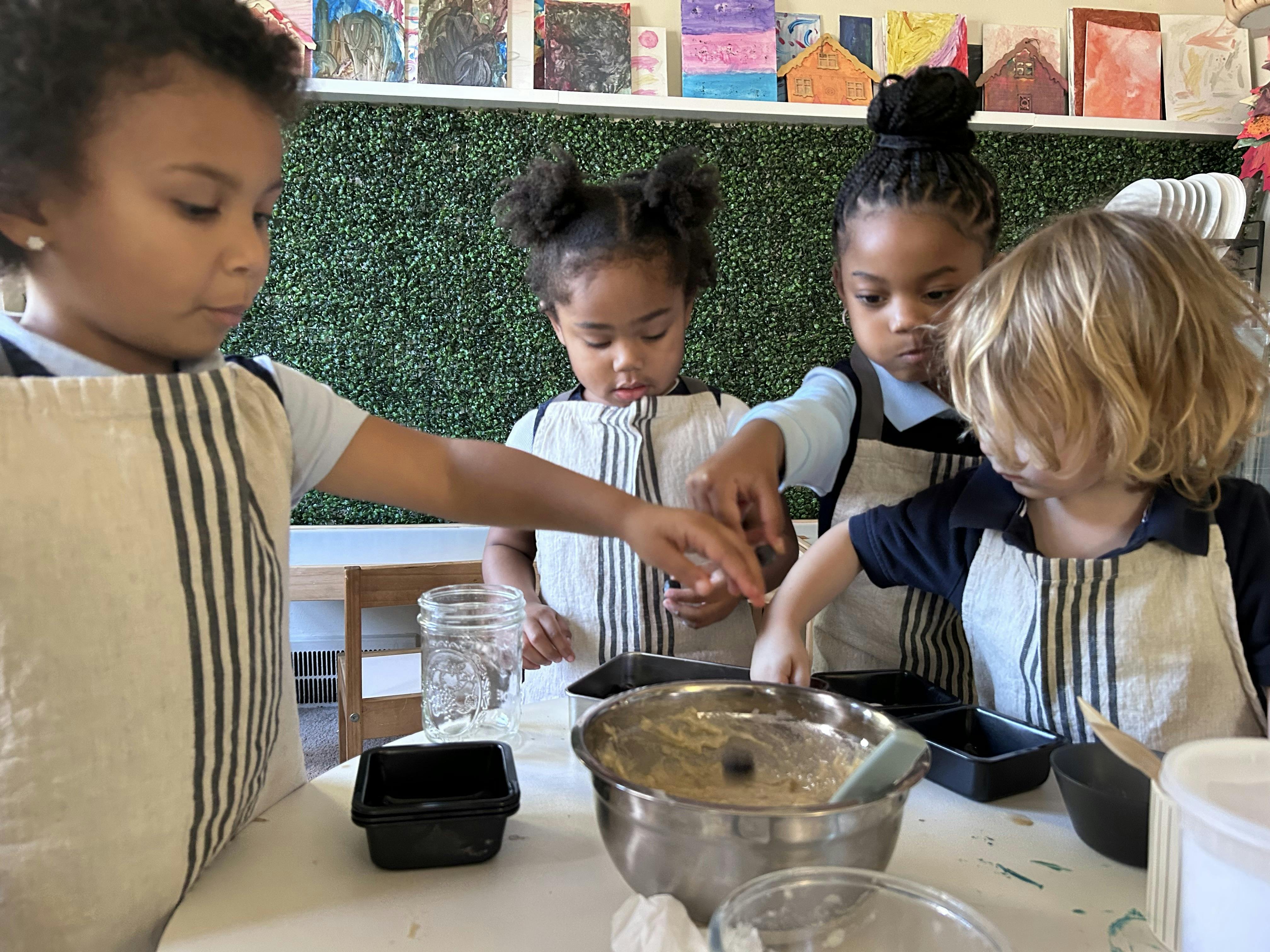 Four children in aprons baking with bowls and pans on a table