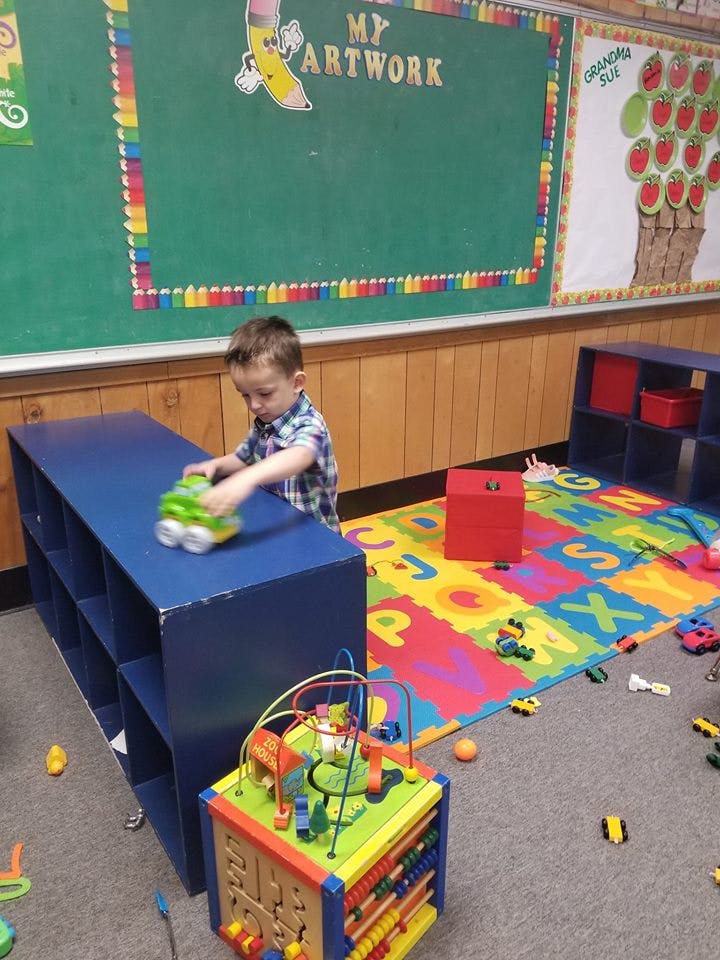Child playing with a toy truck on a blue shelf in a classroom