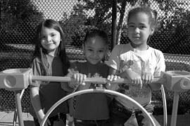 Three children standing behind a play structure