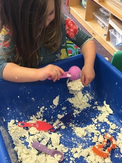 Child playing with kinetic sand in a blue bin