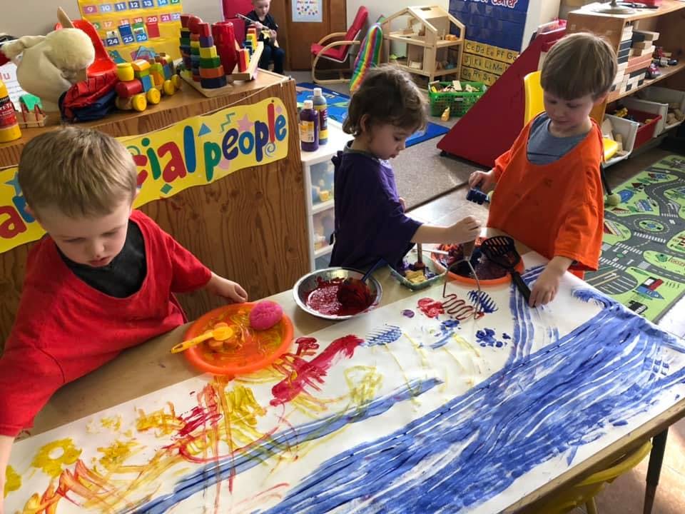 Three children painting on a large sheet of paper on a table