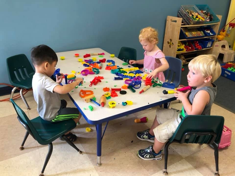 Three children playing with colorful toys at a table in a classroom