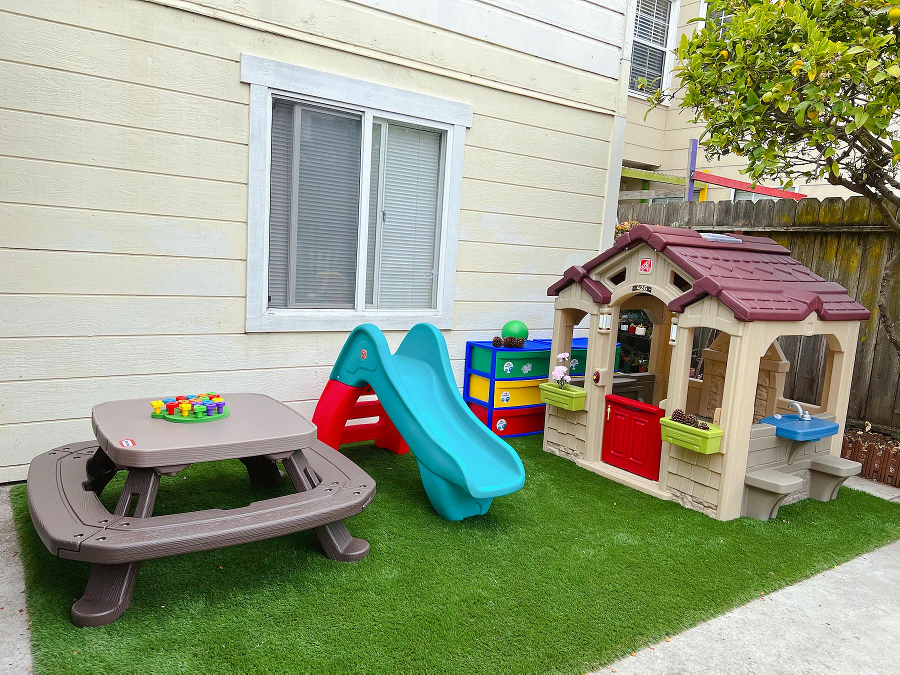 Outdoor play area with a small picnic table, slide, and playhouse