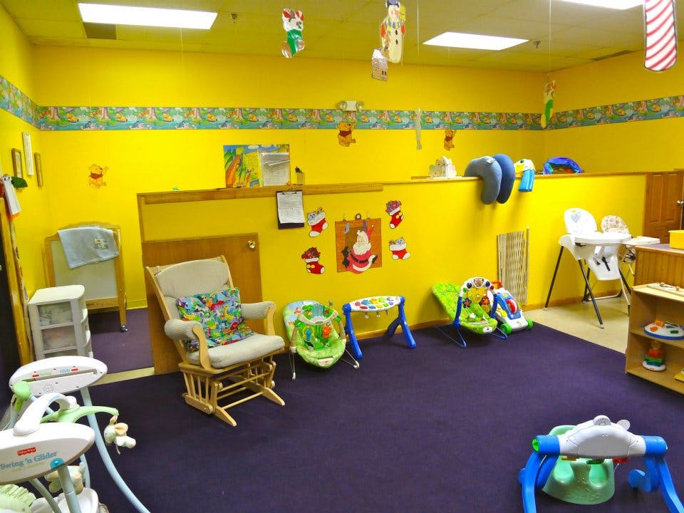 Childcare room with yellow walls, purple carpet, and baby equipment