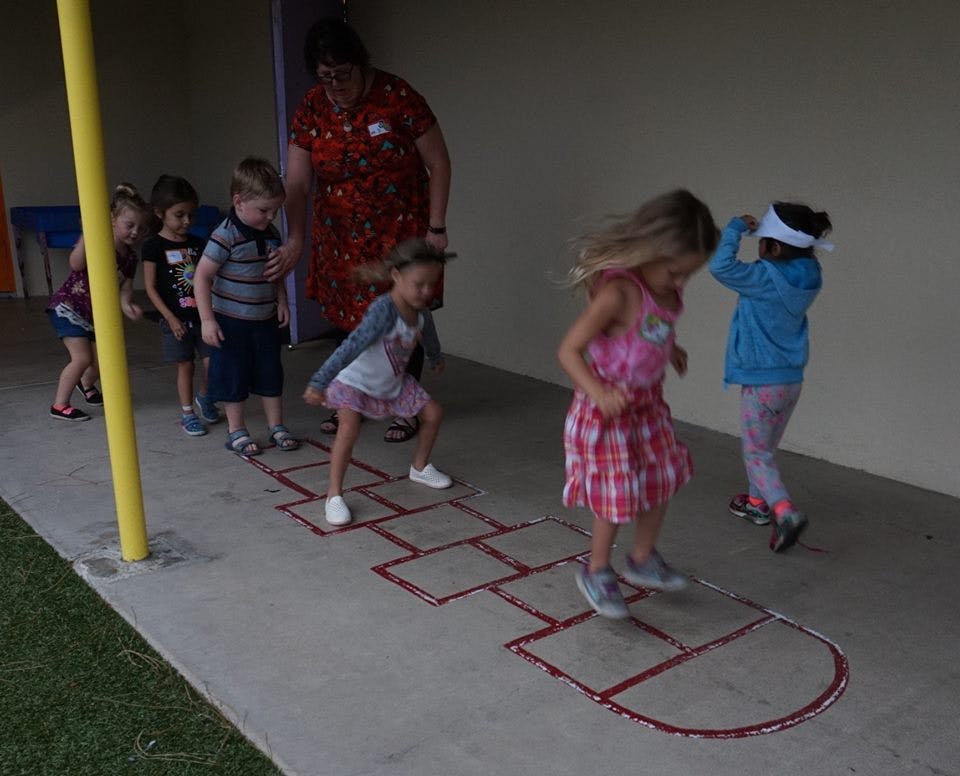 Children playing hopscotch with an adult supervising
