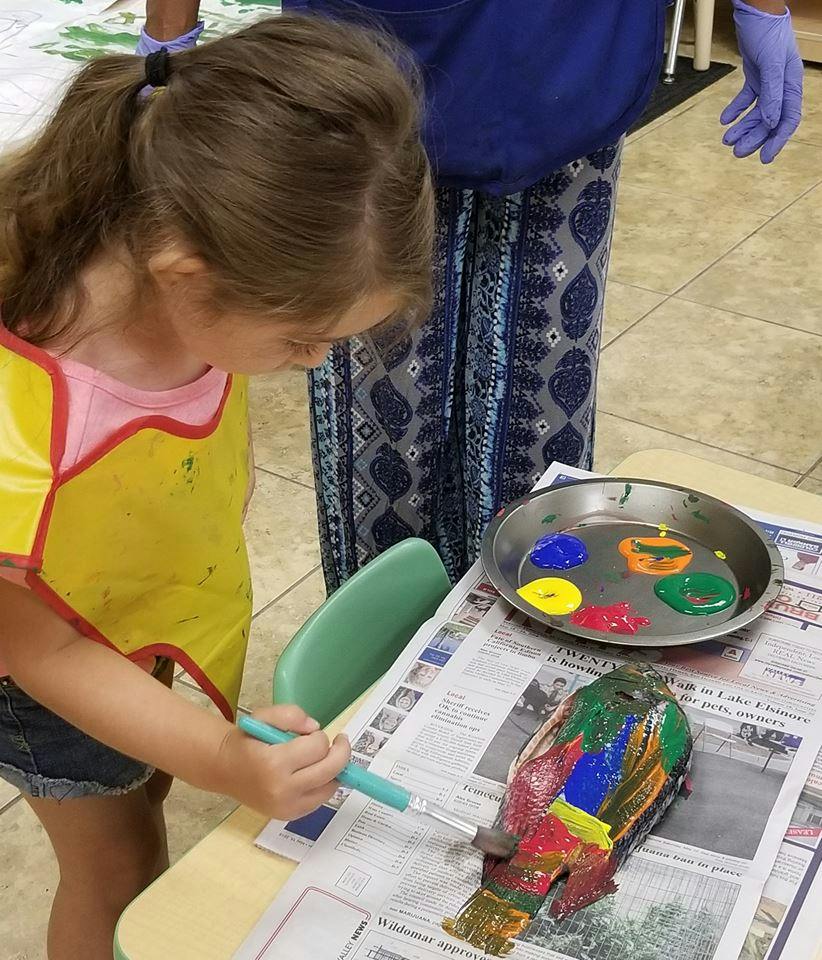 Child painting a colorful bird sculpture on a newspaper-table covered table