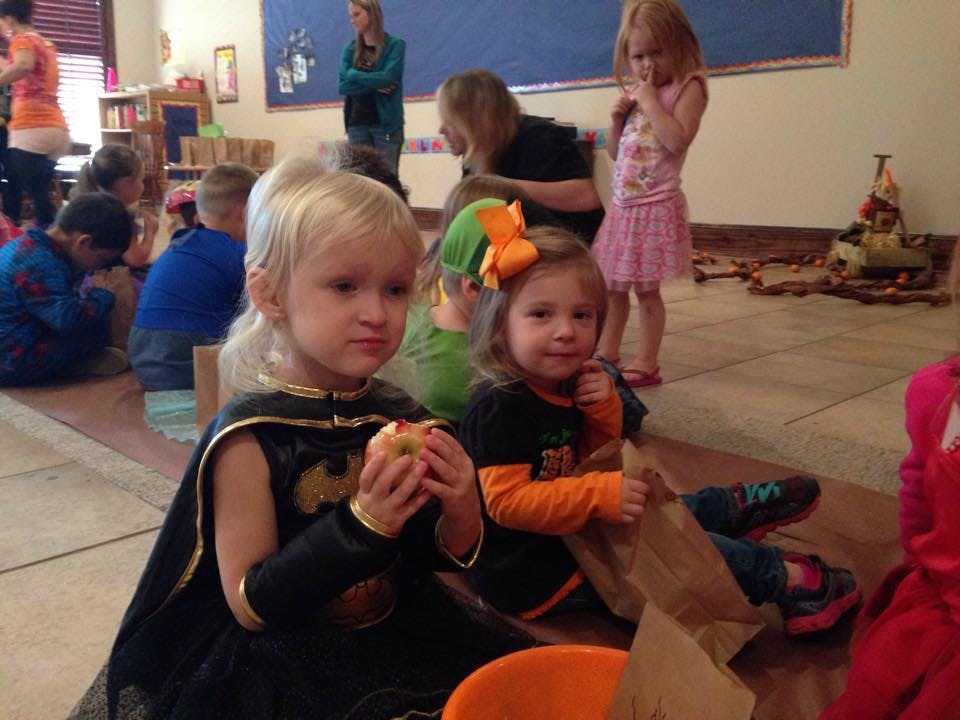Child in Batman costume holding an apple, another child next to them