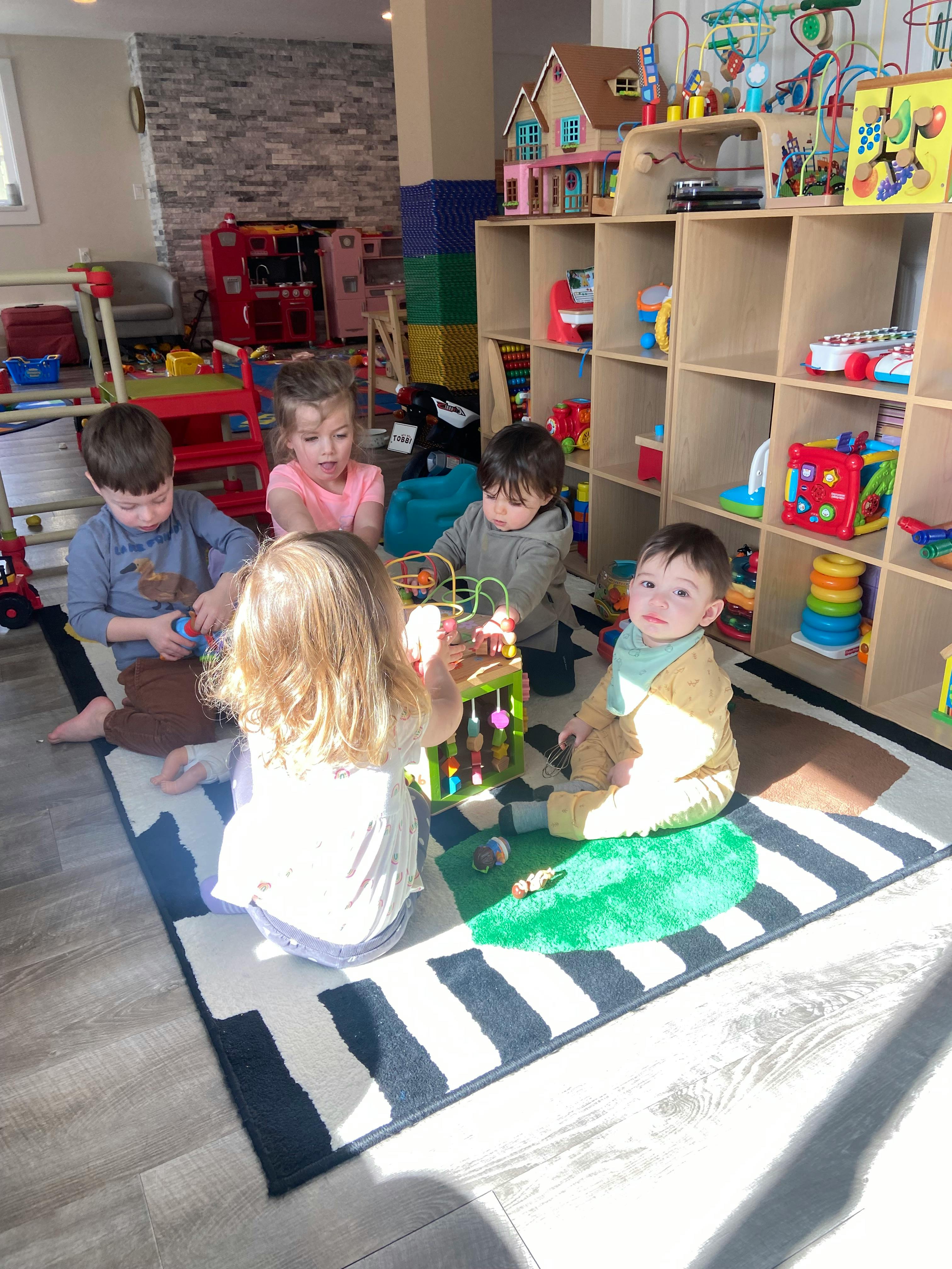 Four children and one baby playing with toys on a rug