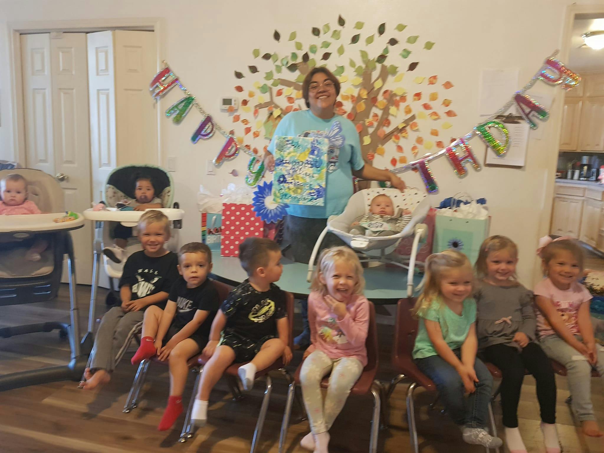 Person holding a gift with multiple children and babies in a room