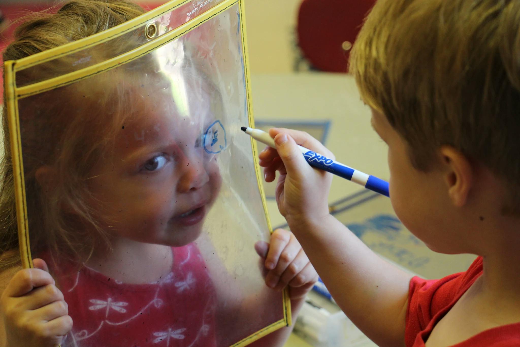 Child drawing on a clear plastic sheet held by another child