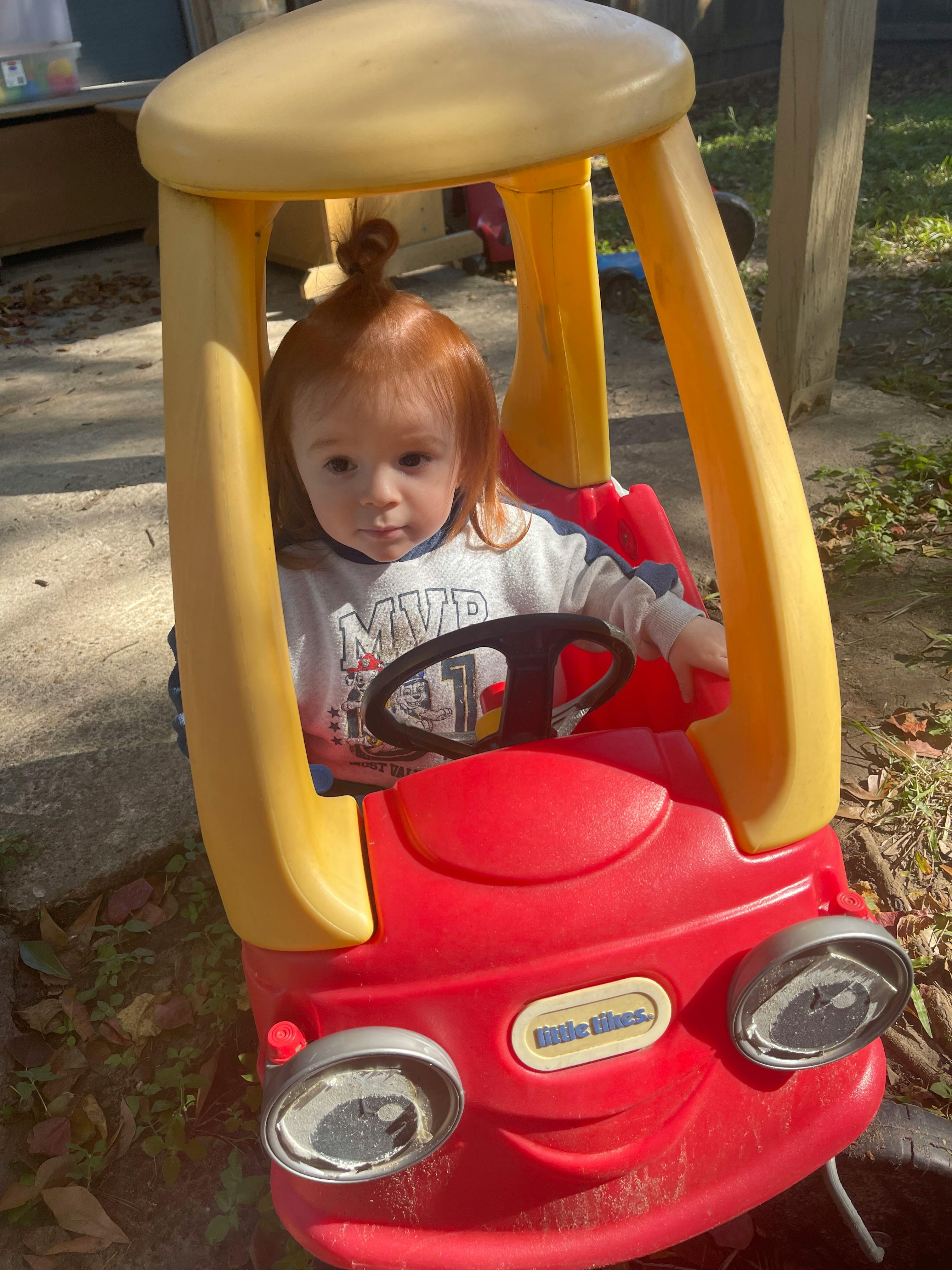 Child with red hair sitting in a red toy car