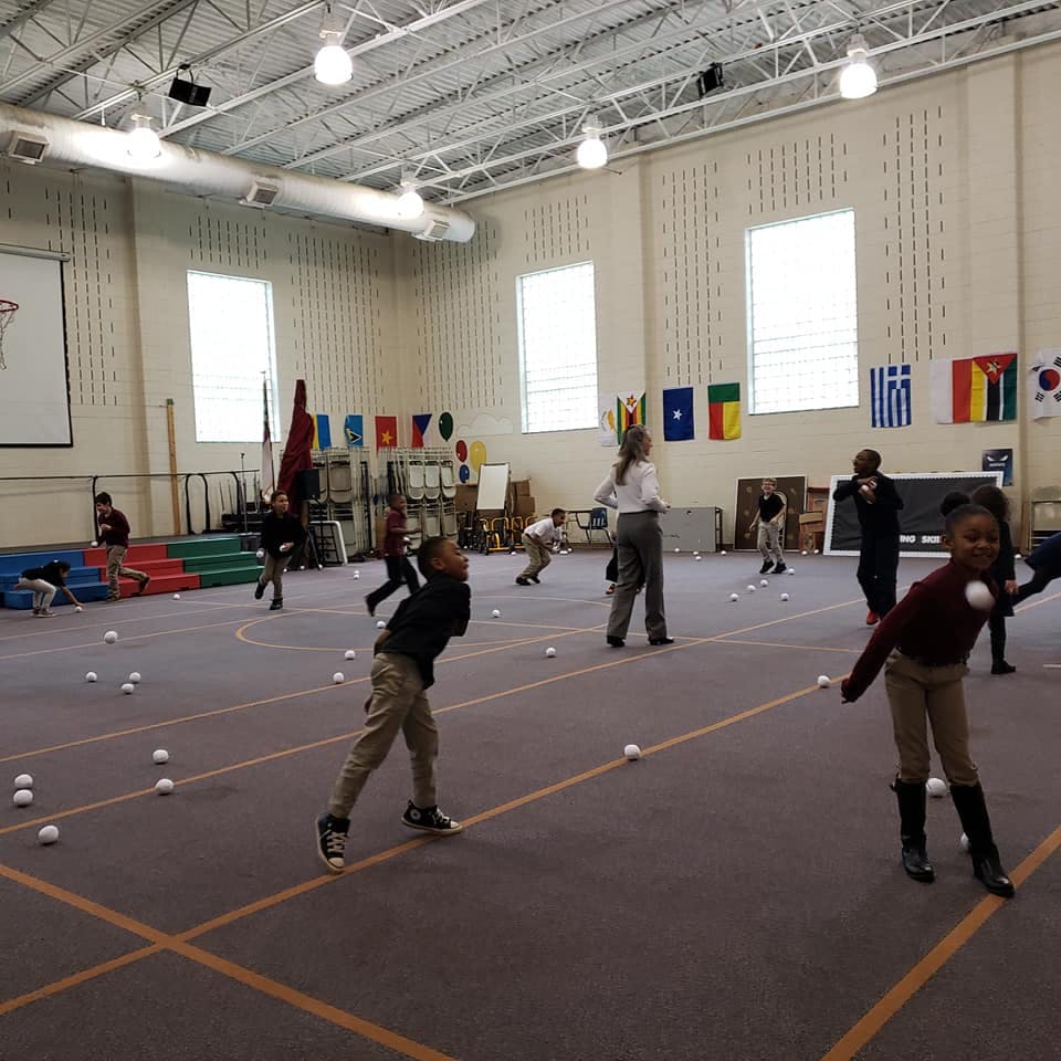 Children and adults playing with softballs in a large indoor space