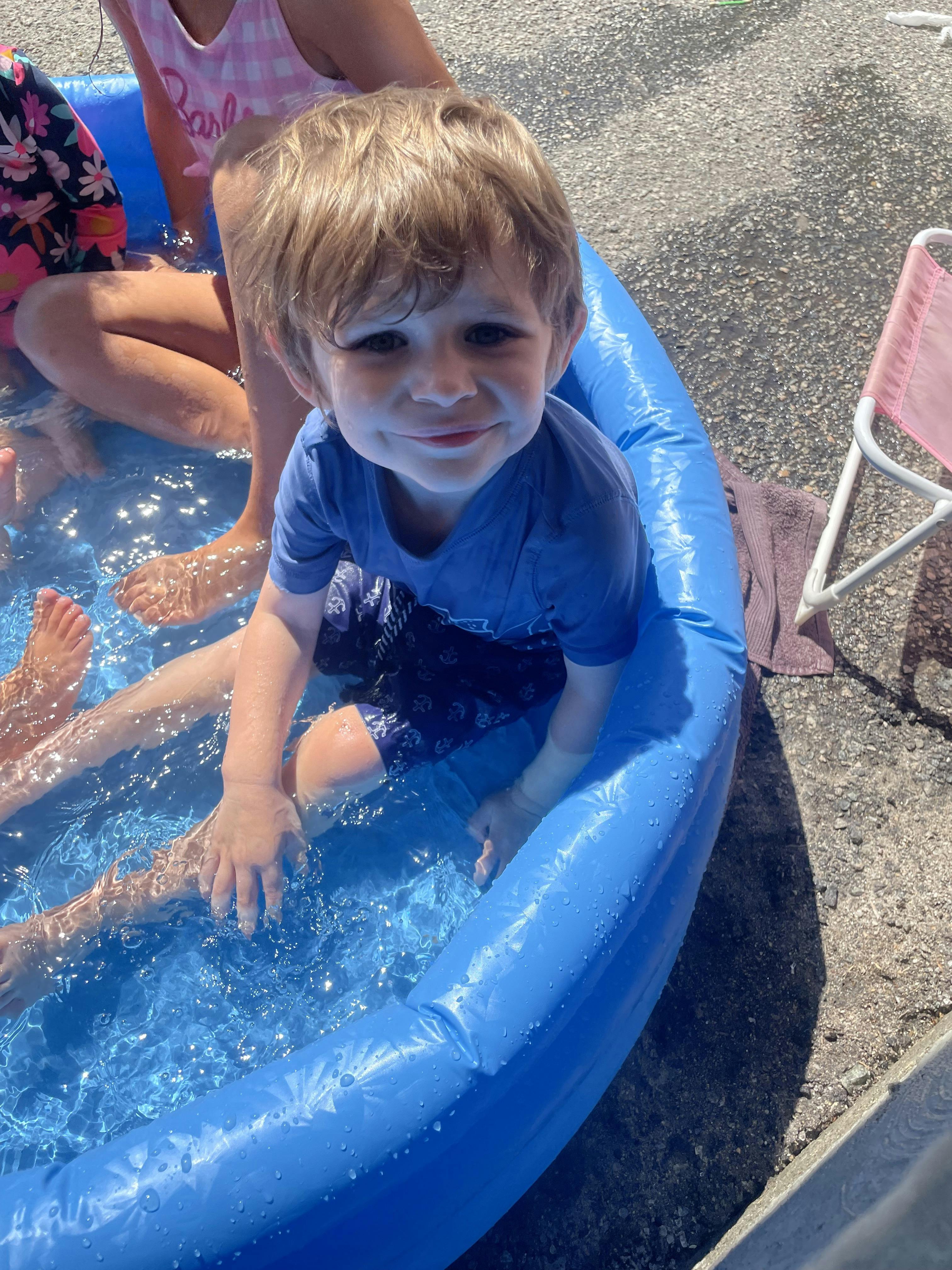 Child sitting in a blue inflatable pool with others