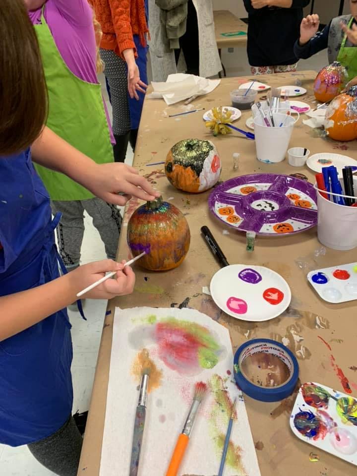 Child painting a pumpkin at a table with art supplies