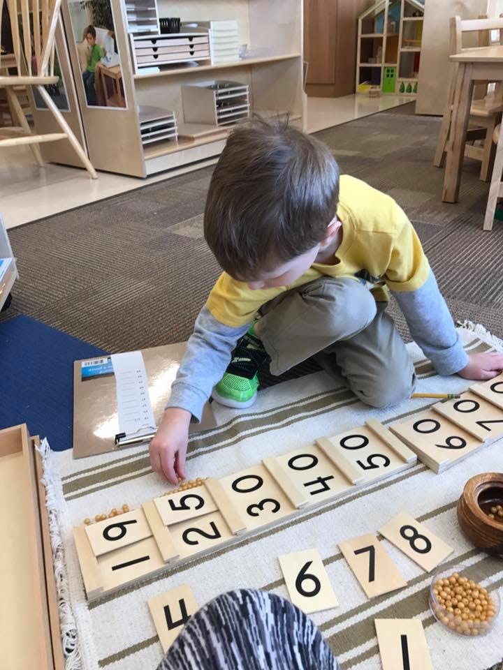 Child on floor arranging wooden number tiles