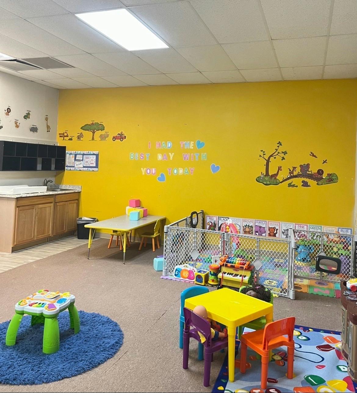 Childcare classroom with small tables, chairs, and play area