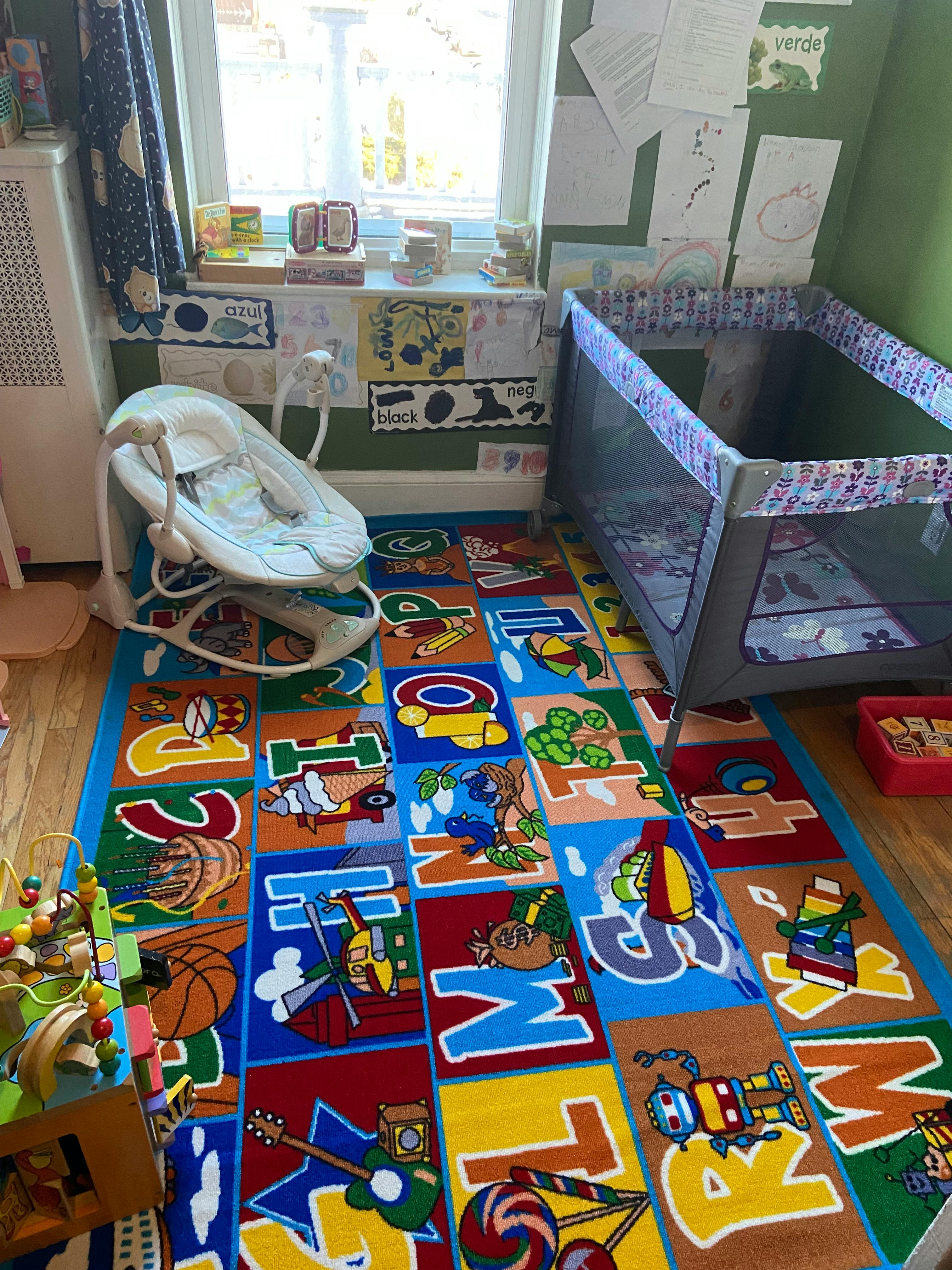 Nursery room with a playpen, baby bouncer, and alphabet rug