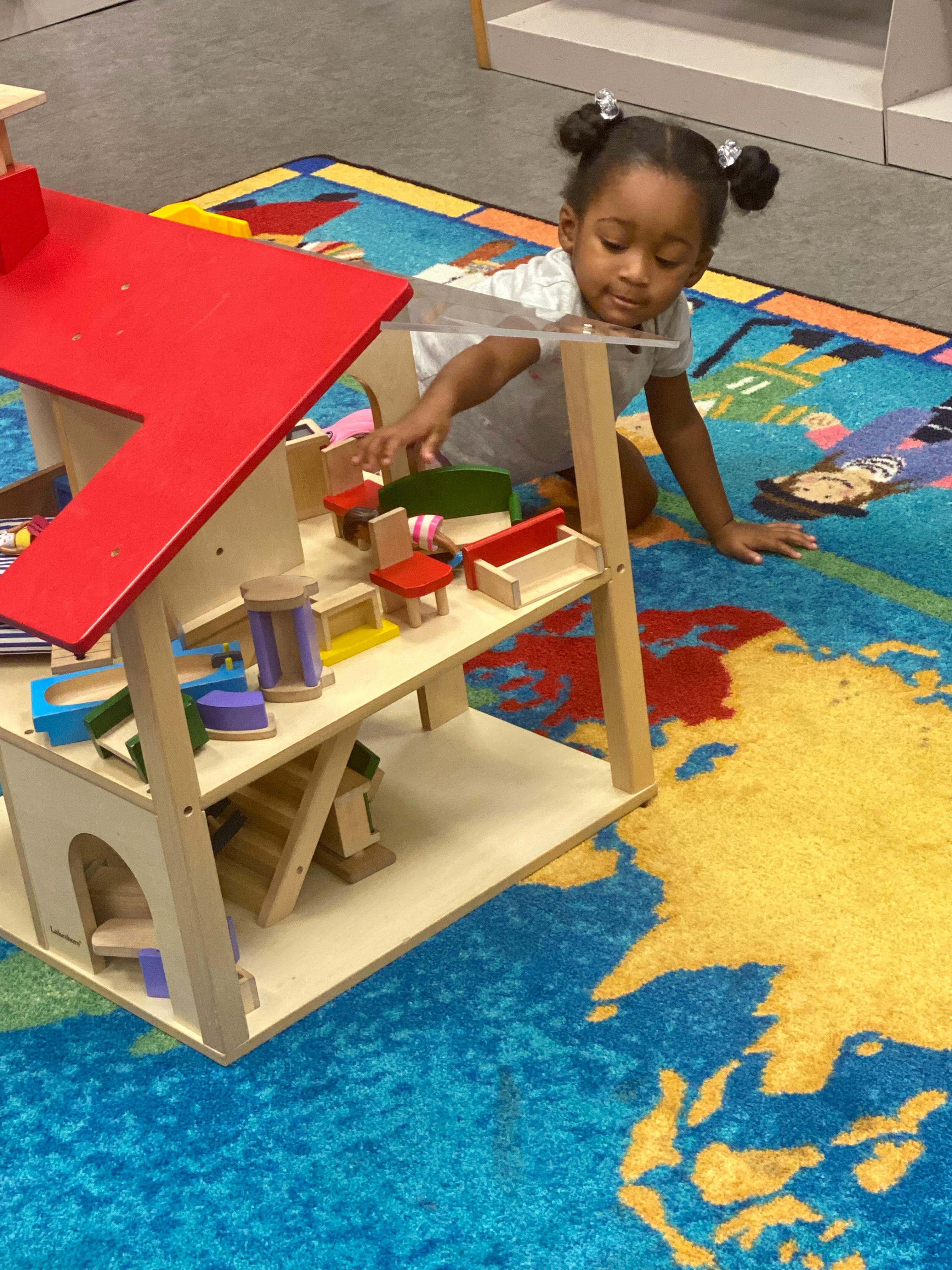 Child playing with a wooden dollhouse on a map-patterned rug