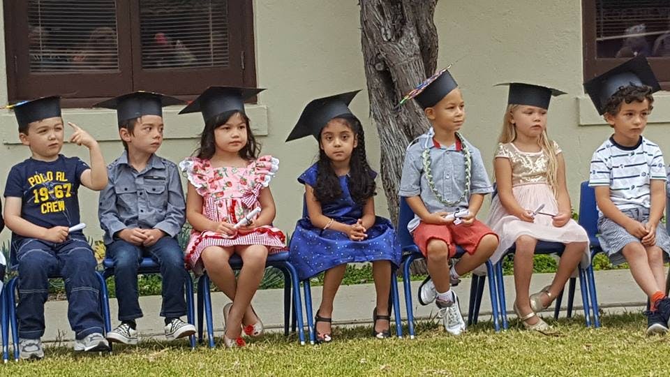 Six children in graduation caps sitting in chairs