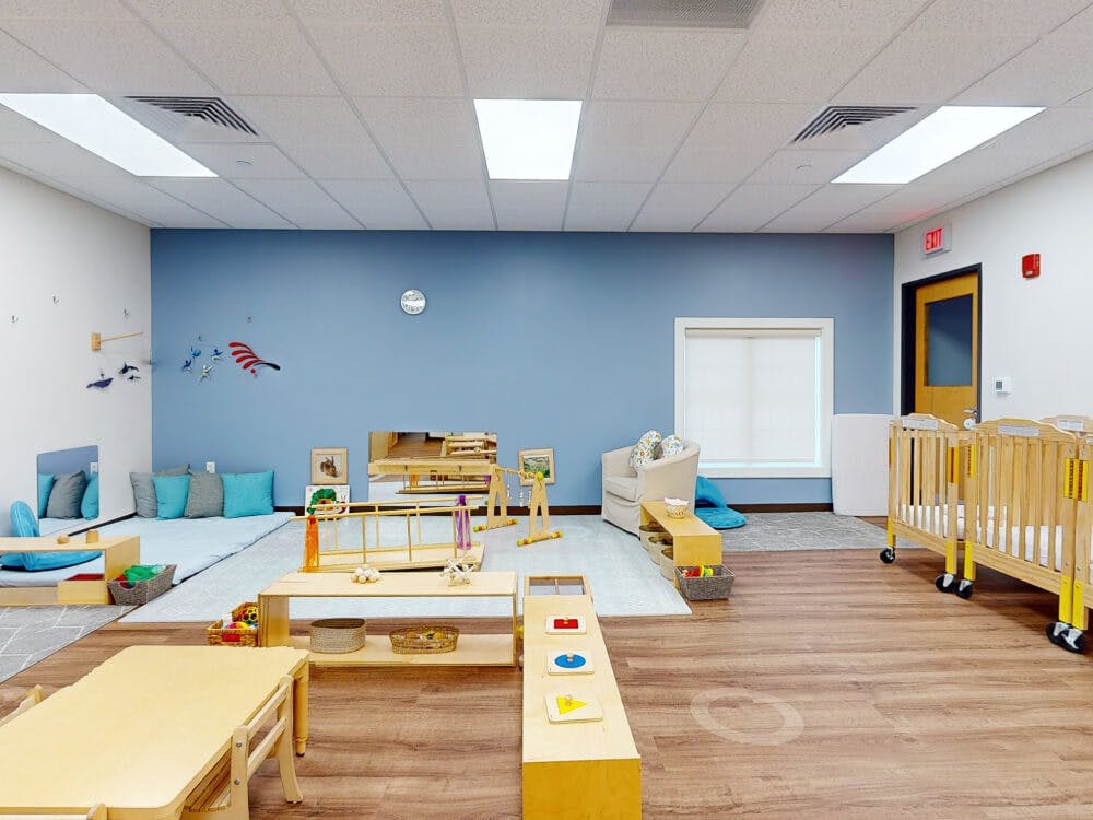 Classroom with low tables, cribs, floor cushions, and educational toys