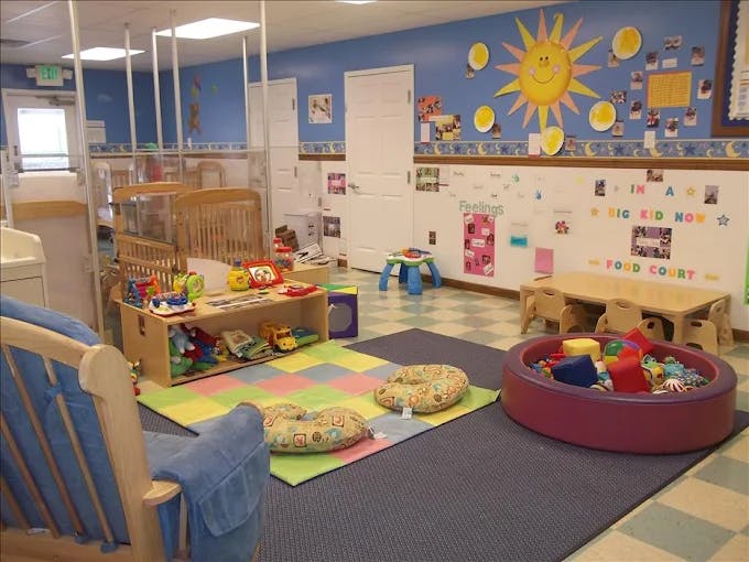 A colorful childcare classroom with cribs, play mats, and a ball pit