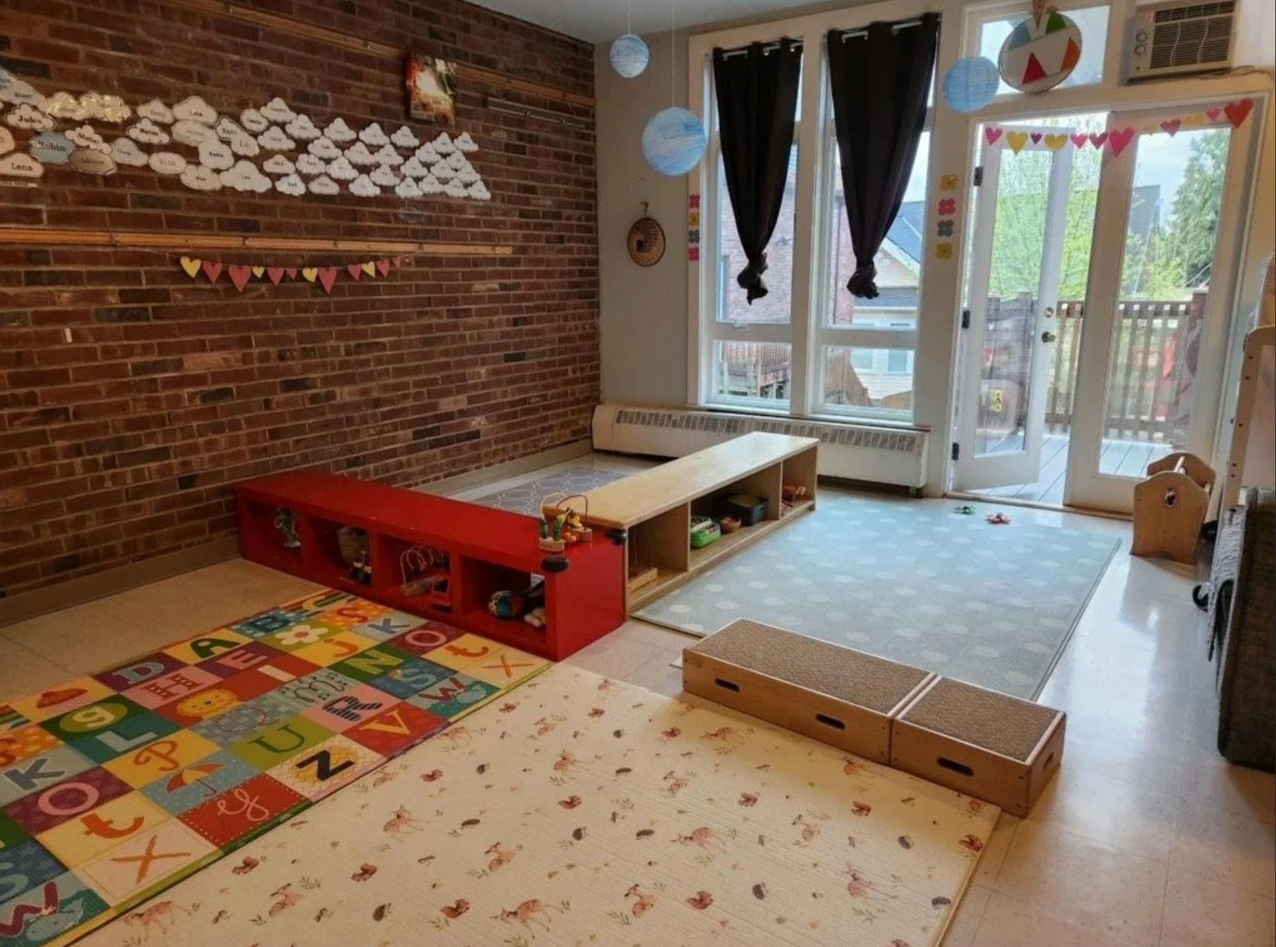 Childcare playroom with rugs, low storage units, and brick wall