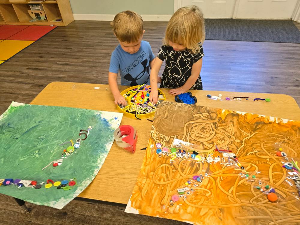 Two children working on art projects with craft supplies at a table