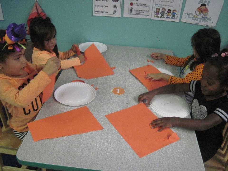 Four children at a table with orange paper and white plates